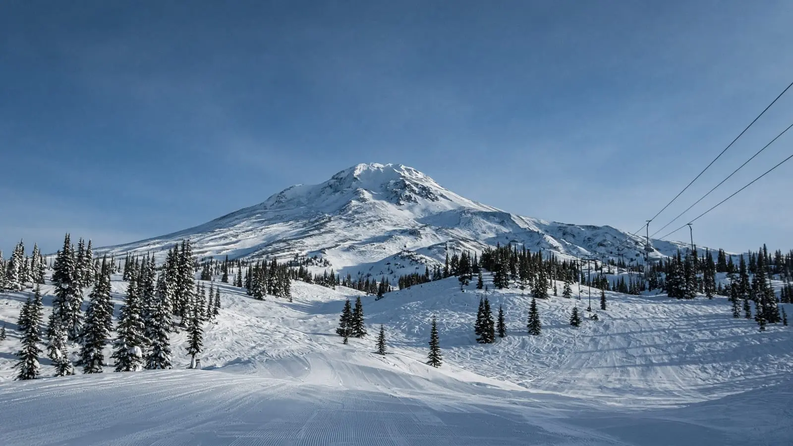 A groomed ski run below a snowy Cascade peak